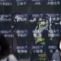 13日、東京都内の株価ボードに反射して写る、マスク姿の人たち（AP＝共同）